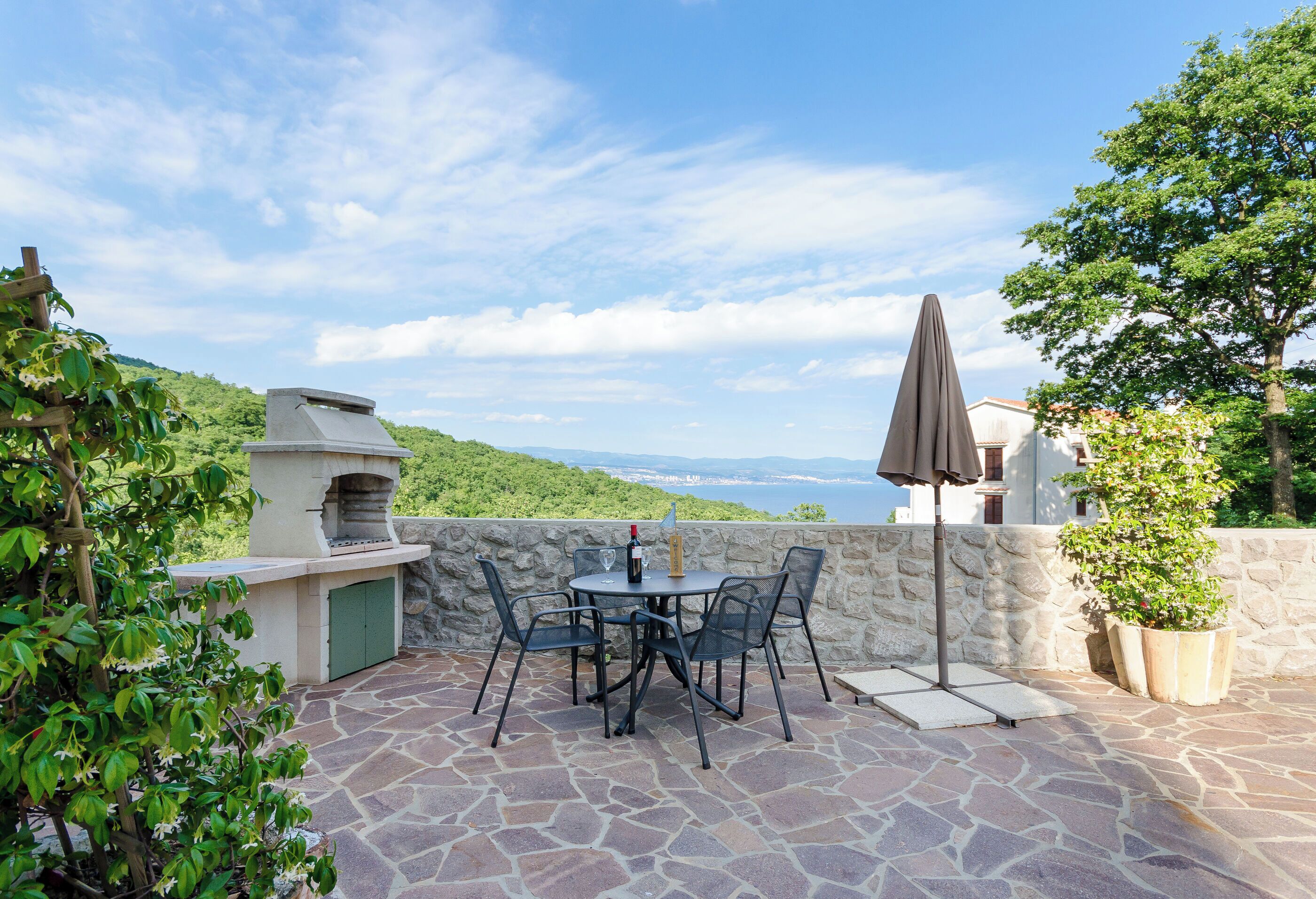 An outdoor patio with stone flooring, a barbecue grill, and a table with chairs.