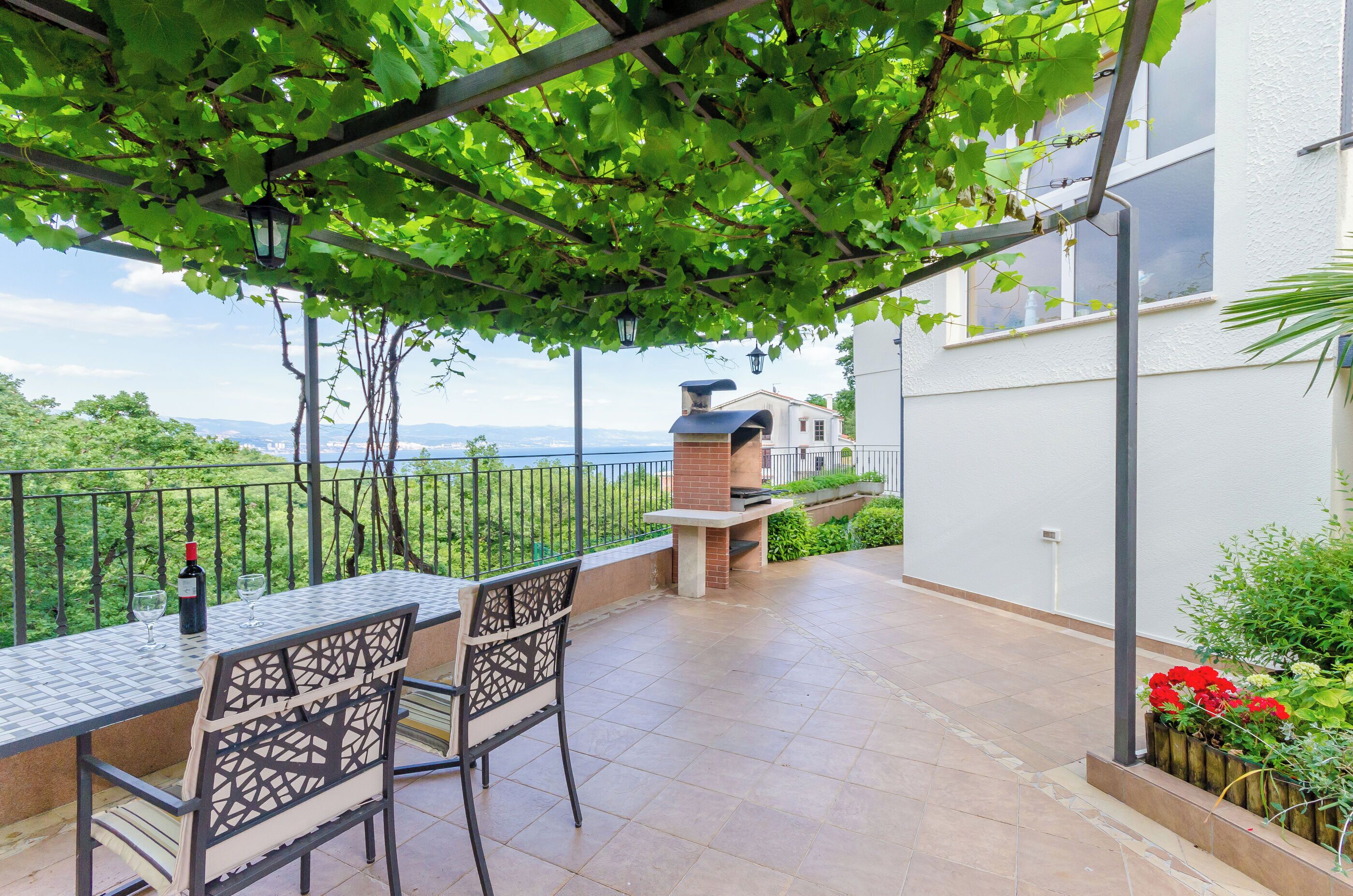 An outdoor patio with a table and chairs, a brick oven, and a view of the sea.