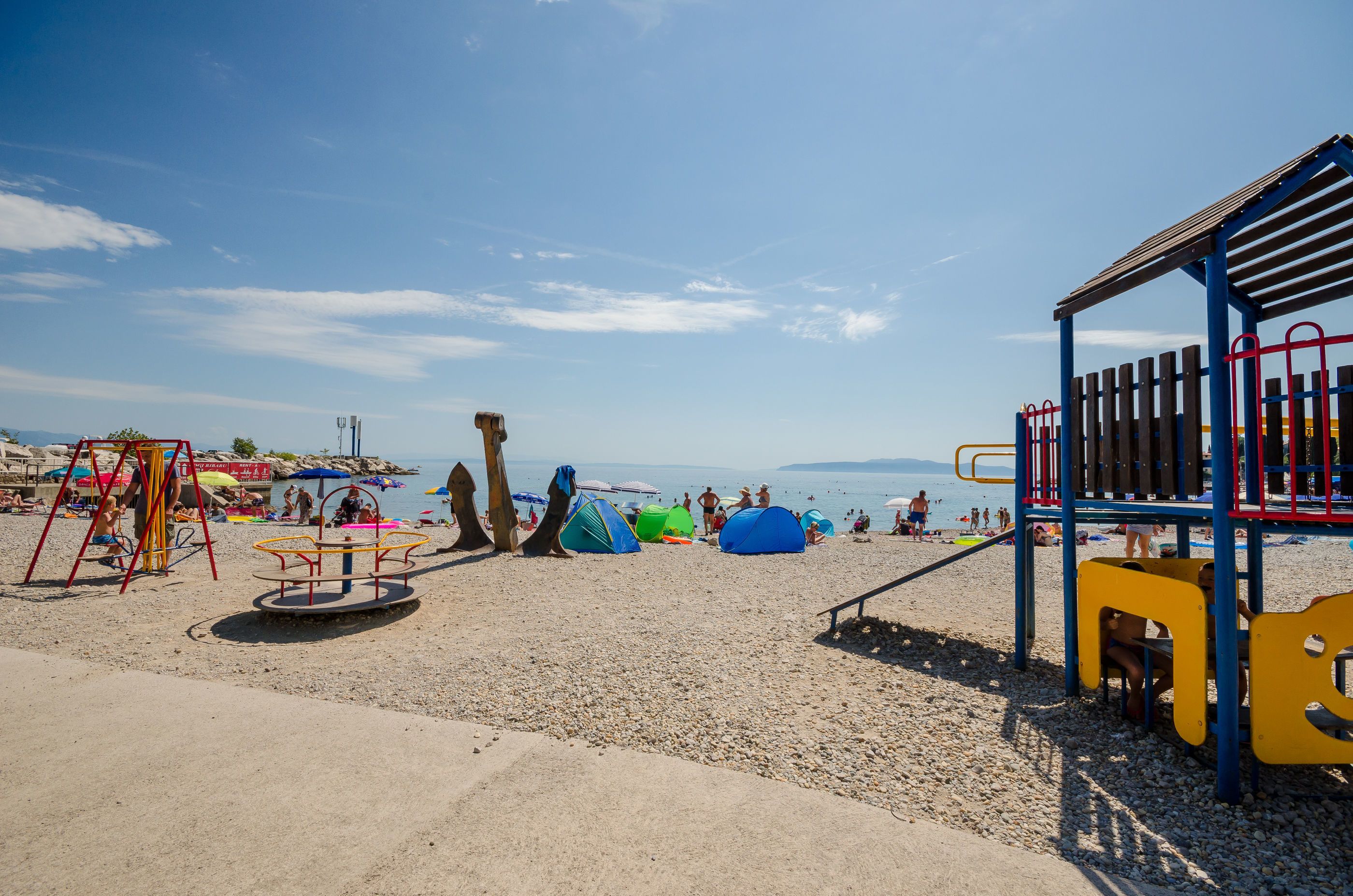 Una spiaggia con un'area giochi, con altalene e strutture per arrampicarsi.