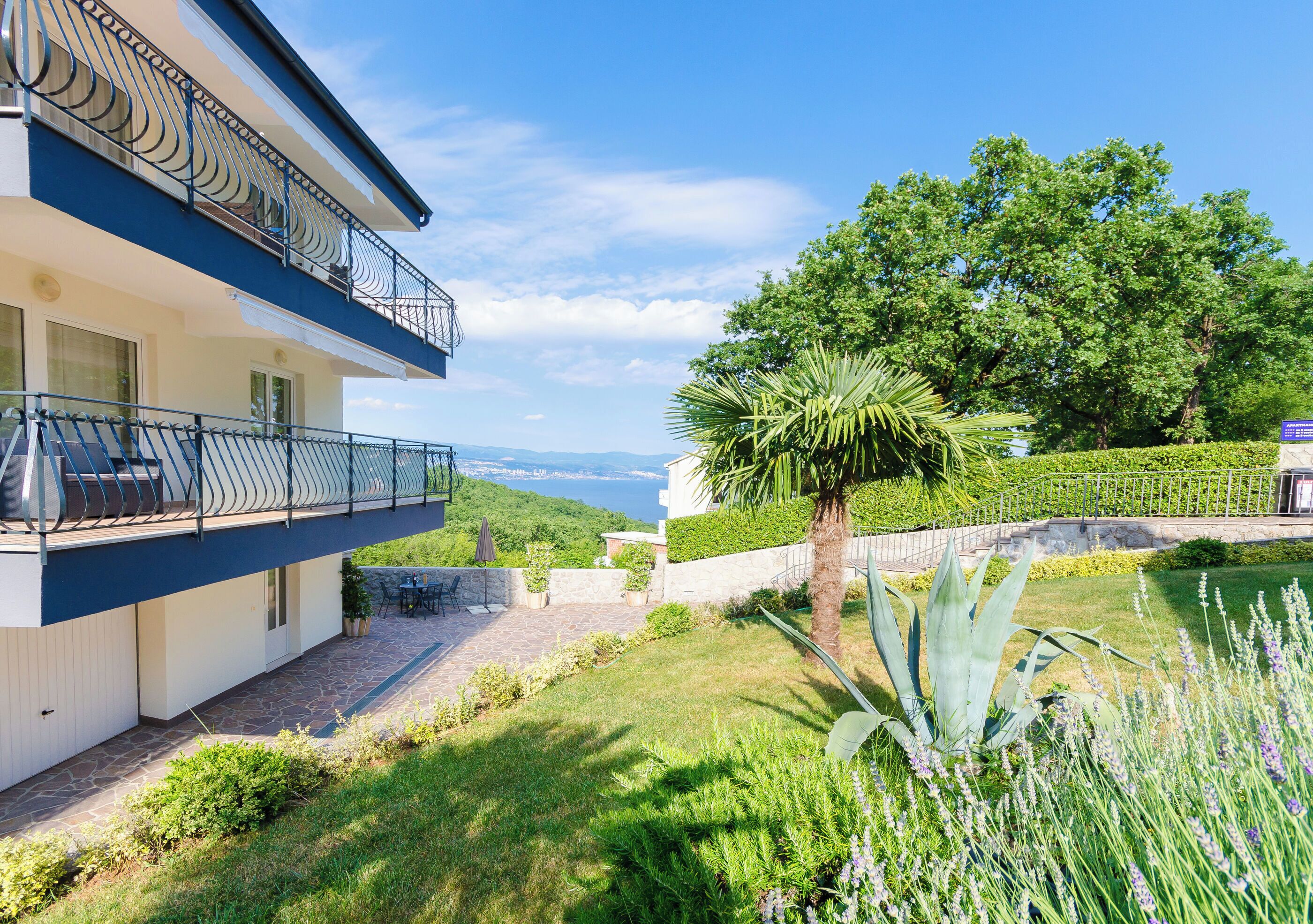 Ein modernes, zweistöckiges Haus mit Balkon, einem gepflegten Garten und Meerblick.