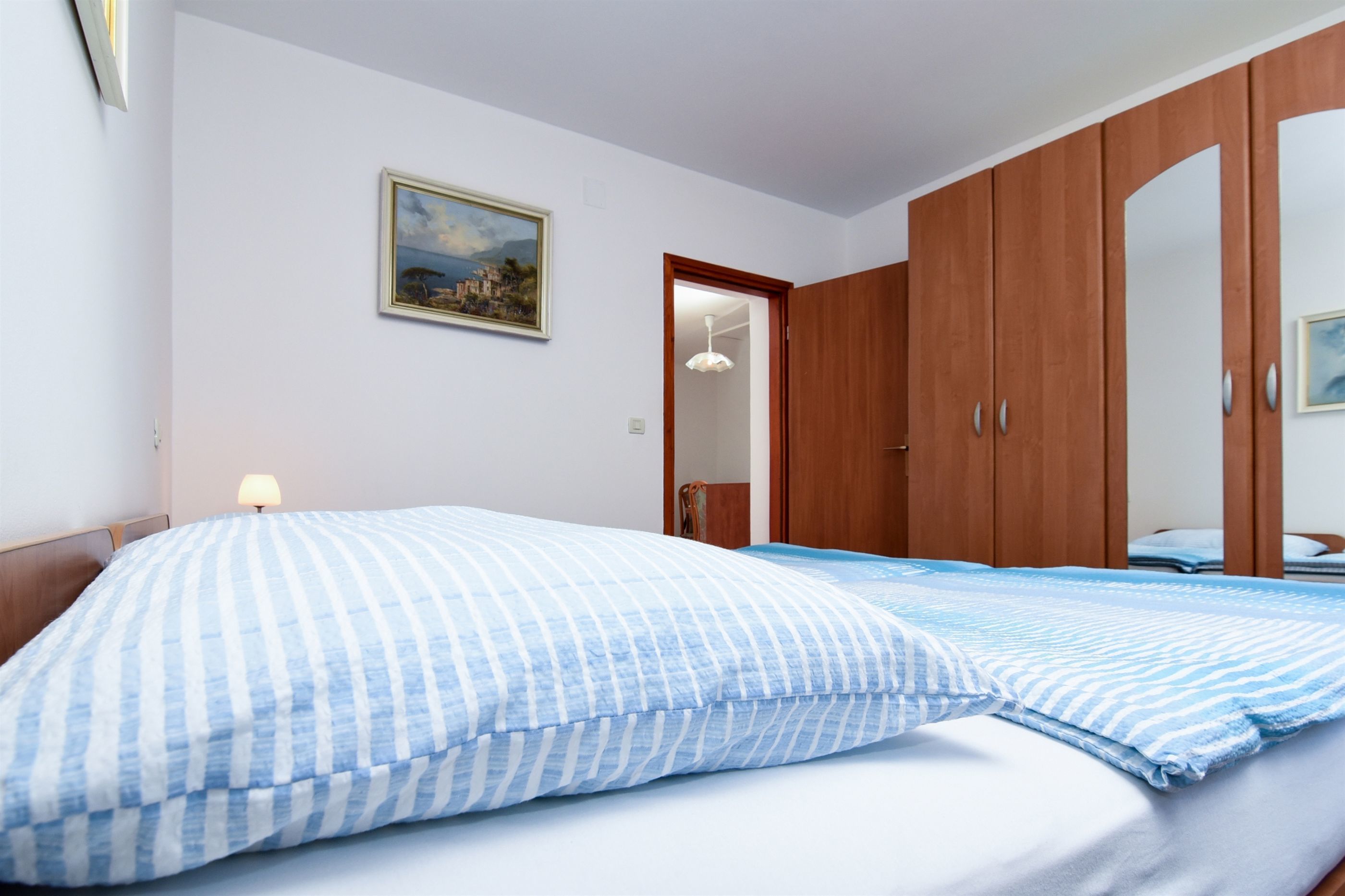 Een slaapkamer met een bed, een houten garderobe, een schilderij aan de muur en een deur naar een andere kamer.