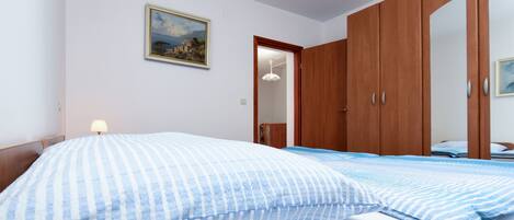Een slaapkamer met een bed, een houten garderobe, een schilderij aan de muur en een deur naar een andere kamer.