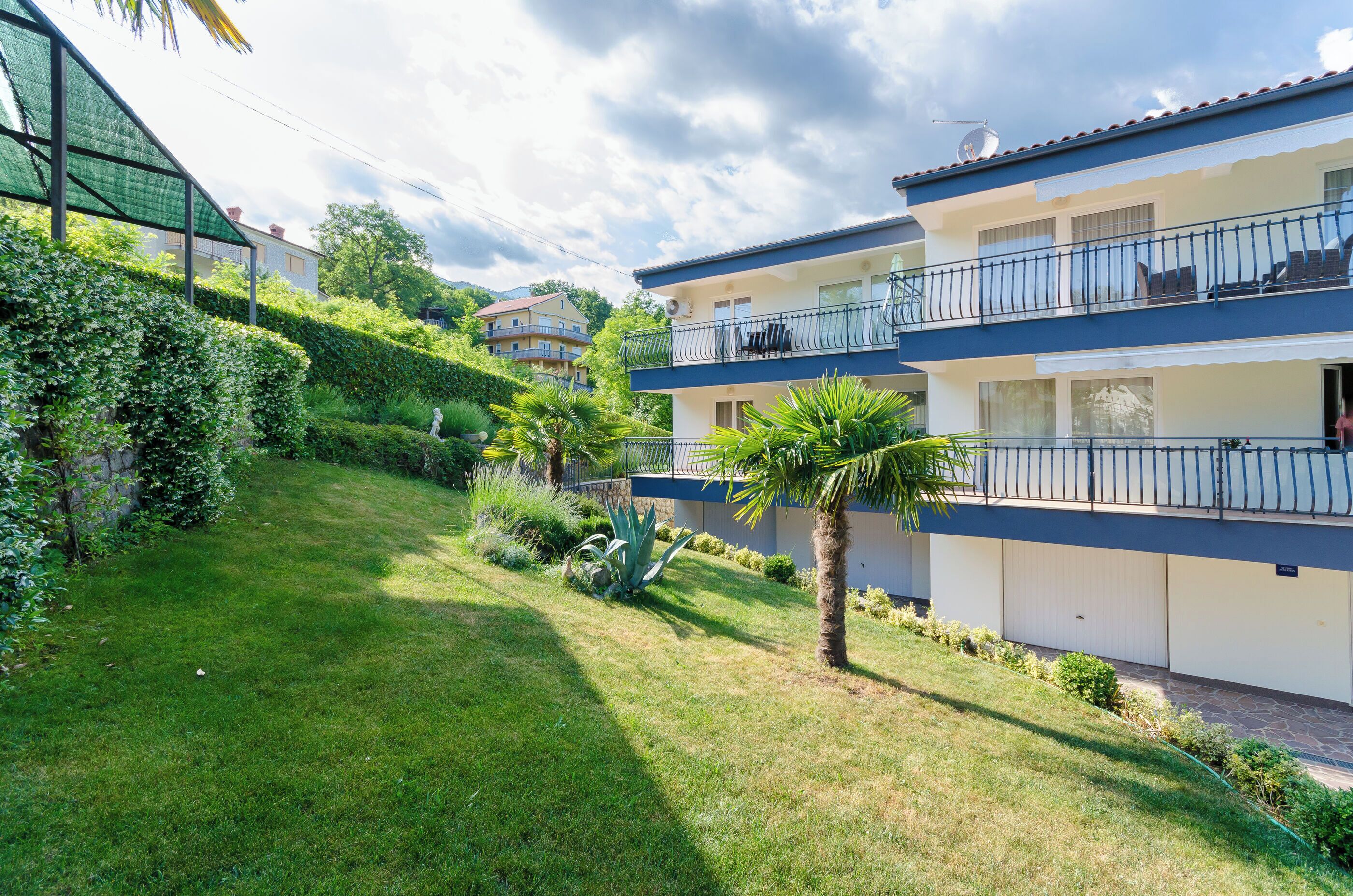 Un edificio residenziale a più piani con balconi, un prato curato e vegetazione circostante.