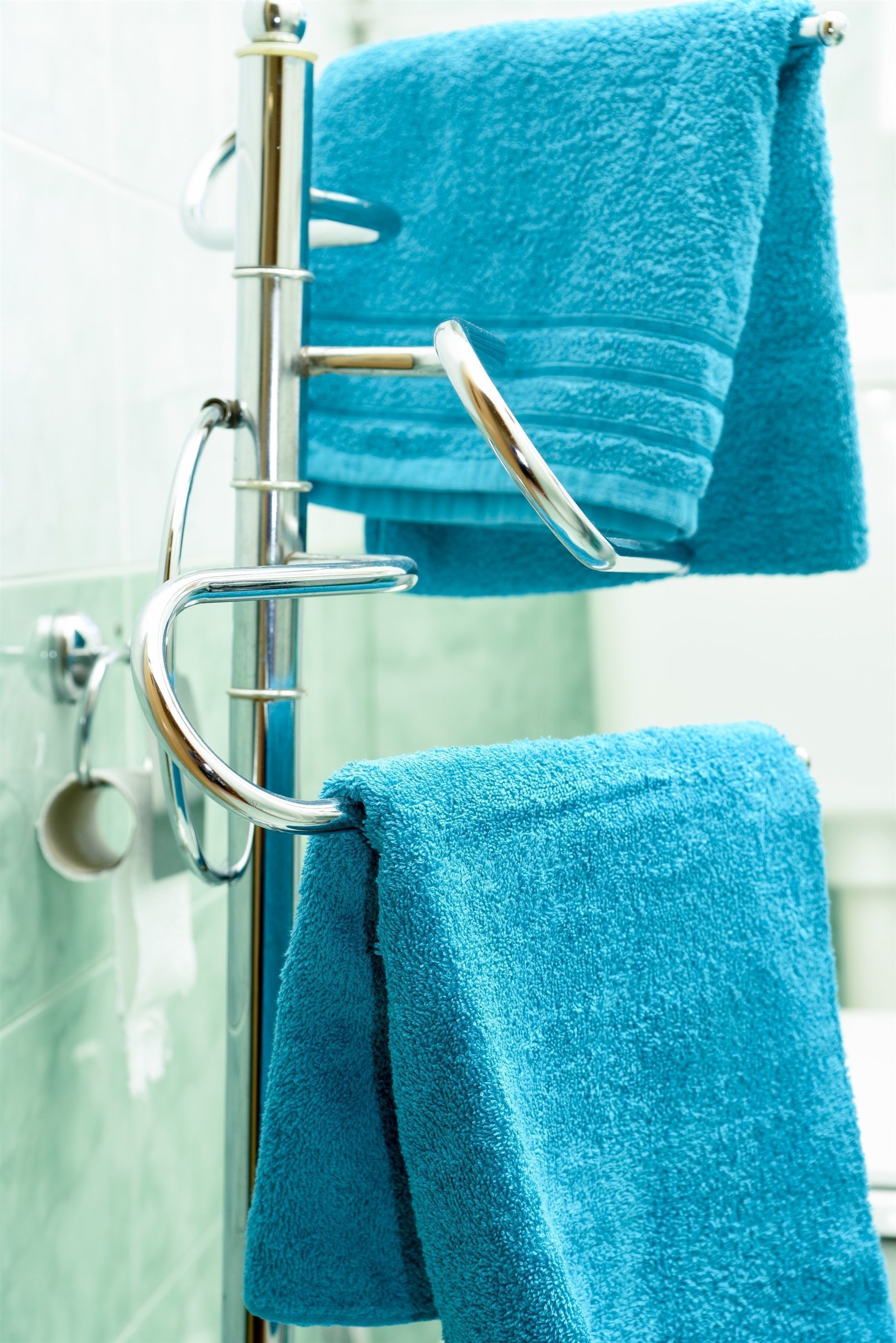 A bathroom with a chrome towel rack holding two blue towels.
