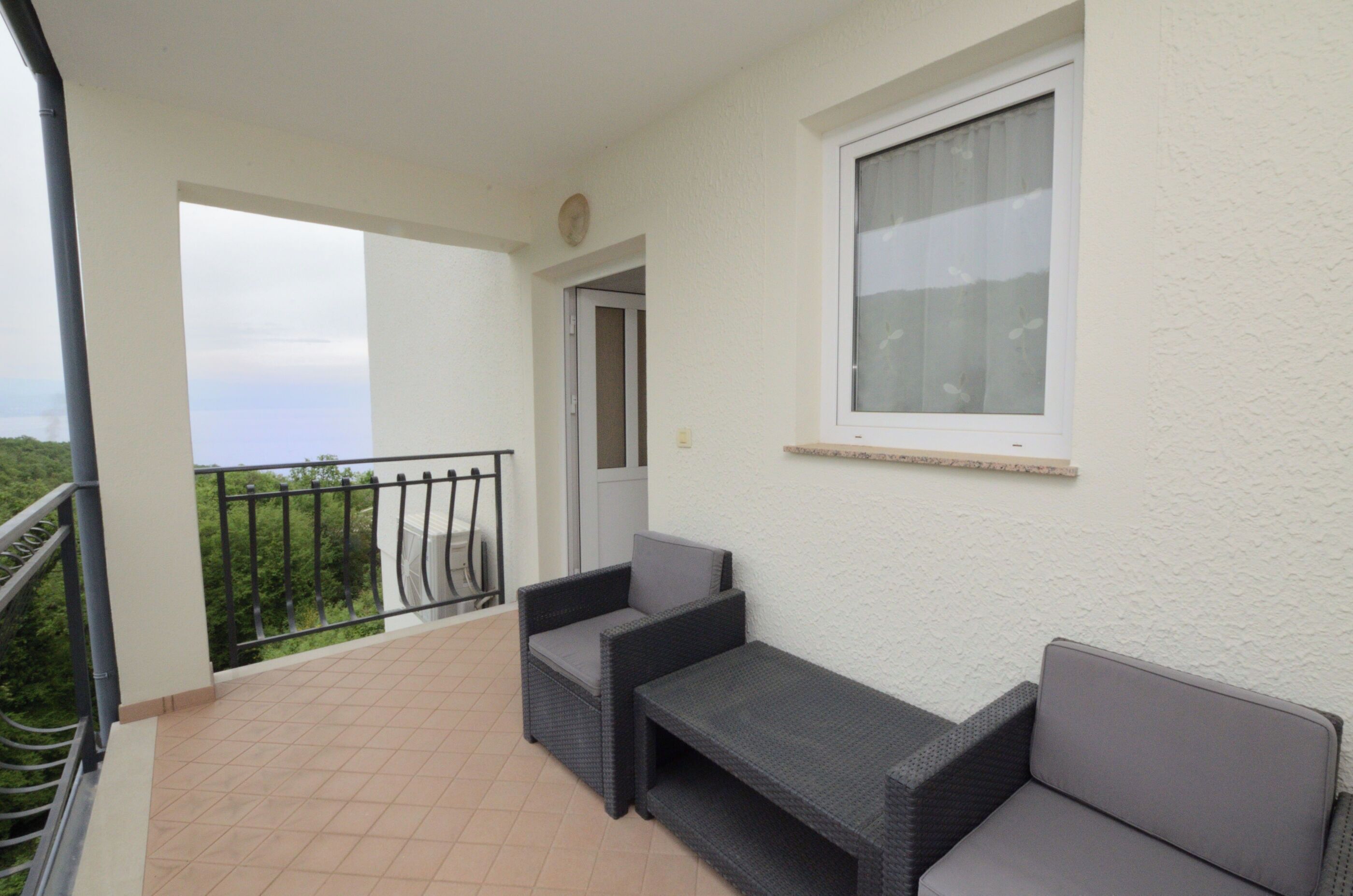 A balcony with two wicker sofas and a small table, a window with a curtain, and a door leading to the interior.