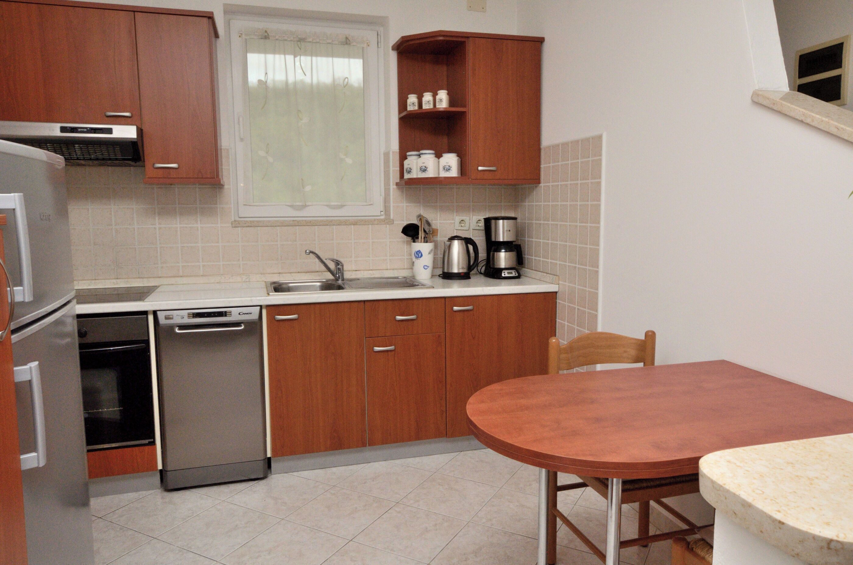 A compact kitchen with wooden cabinets, a dishwasher, a coffee maker, and a dining table.