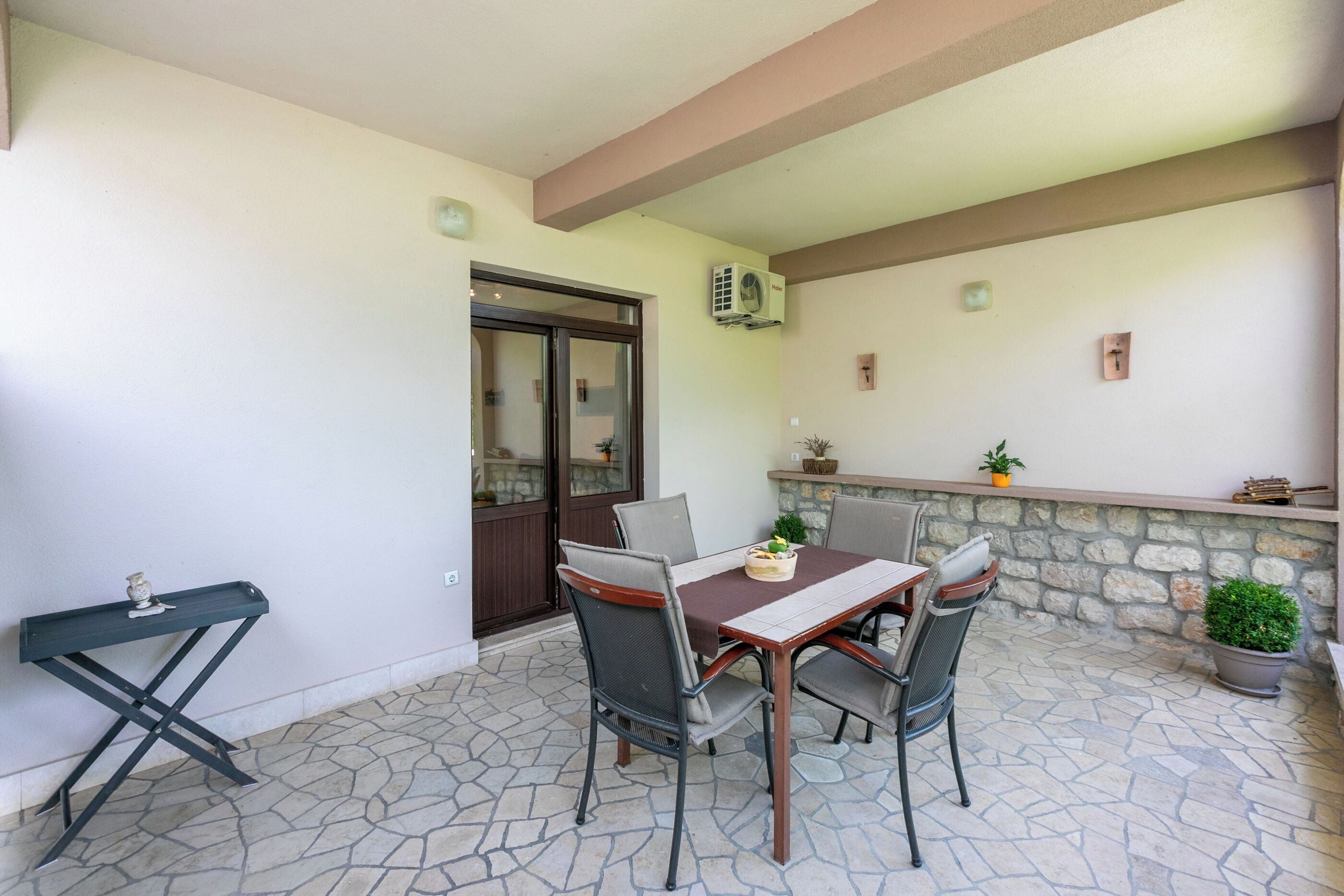 Eine Terrasse mit Tisch und Stühlen, einem kleinen Beistelltisch und einer Steinmauer mit Pflanzen.