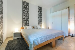 A bedroom with a bed, nightstand, wardrobe, and a large window. - Apartment Milojka (Crikvenica)