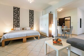 A modern bedroom with a bed, bedside table, and a dining area with chairs and a table. - Apartment Milojka (Crikvenica)
