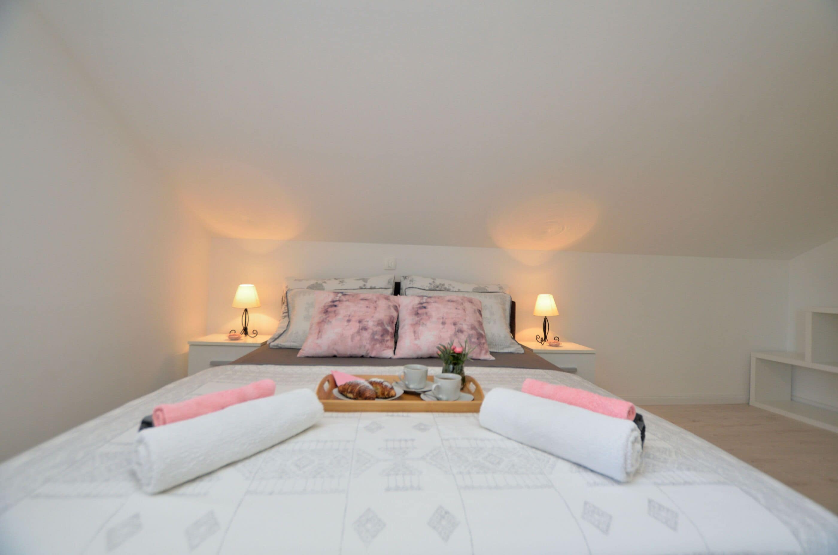A neatly made bed with a tray of breakfast items, two bedside lamps, and a bedside table with a lamp.