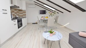 A modern kitchen with white cabinets, a built-in oven, and a dining area with a table and chairs. - Apartments Viktoria (Lovran)