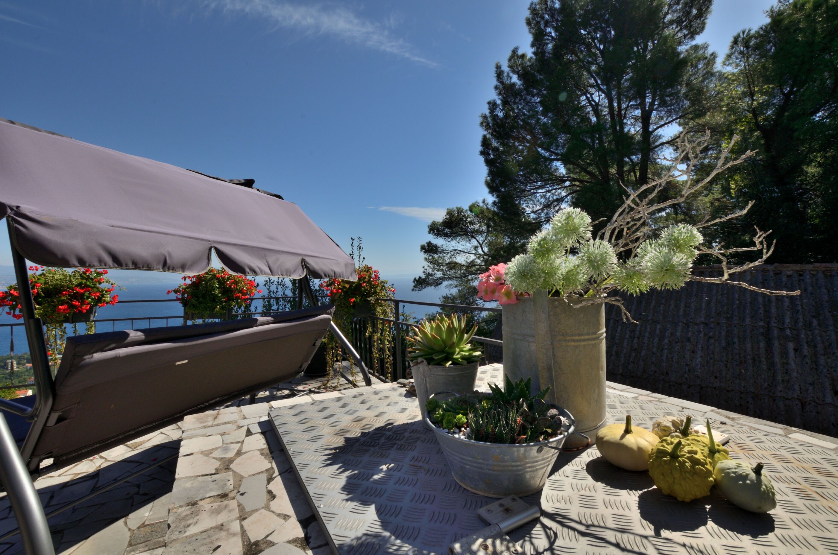 A terrace with a view of the sea, outdoor seating, potted plants, and a table with pumpkins.
