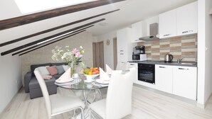A modern kitchen with white cabinets, a black oven, and a coffee maker. There is a dining table with chairs and a vase of flowers. - Apartments Viktoria (Lovran)