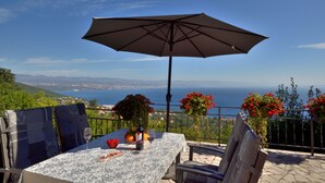 A terrace with a table, chairs, and an umbrella overlooking a scenic view. - Apartments Viktoria (Lovran)