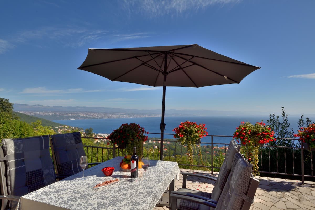 Terraço com mesa, cadeiras e guarda-sol, com vista panorâmica.