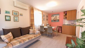 A living room with a sofa, dining table, chairs, and a kitchen area with cabinets and a sink. - Apartment Paulina (Cres)