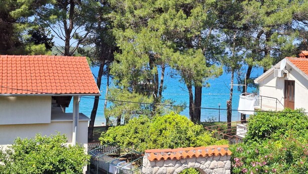 A coastal building with a tiled roof, surrounded by trees and a clear view of the sea. - Apartment Paulina (Cres)