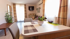 A dining area with a table, chairs, a potted plant, and a television on the wall. - Apartment Paulina (Cres)