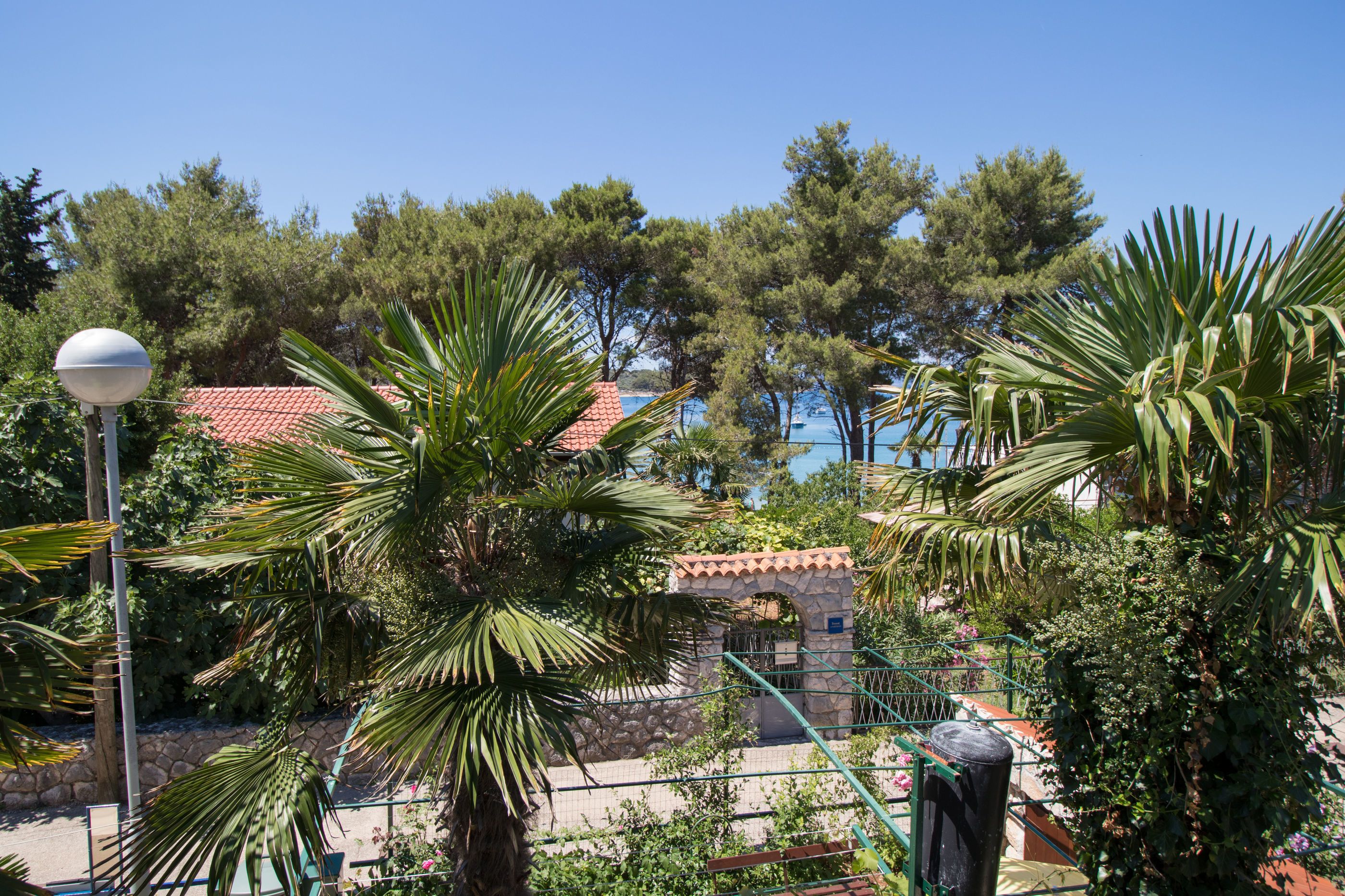 A coastal building with a red-tiled roof, surrounded by lush greenery and a clear blue sky.