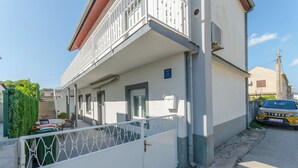 A two-story building with a balcony, a gated entrance, and a parked car. - Apartments Danica (Pirovac)