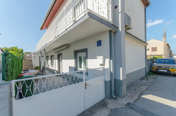 A two-story building with a balcony, a gated entrance, and a parked car.