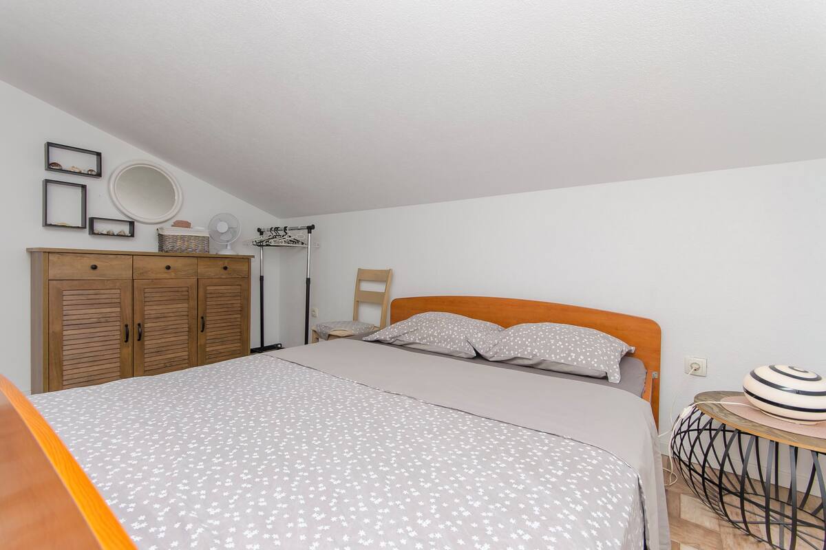 Een slaapkamer met een bed, een houten garderobe, een spiegel en een nachtkastje.