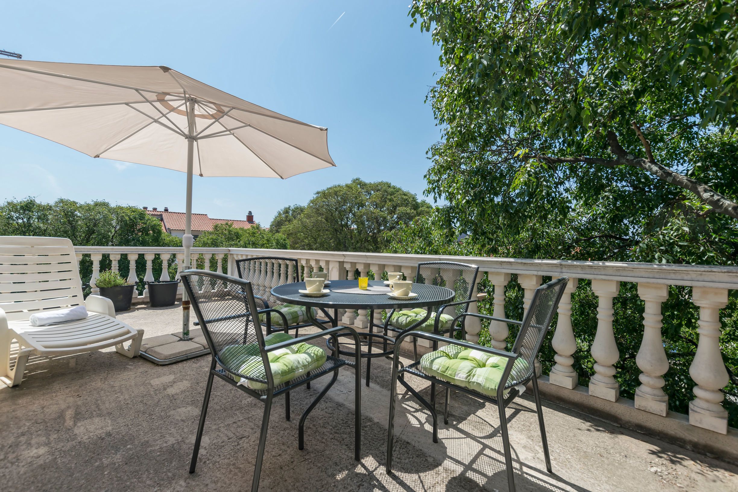 Een terras buiten met een ronde tafel, stoelen en een grote parasol.