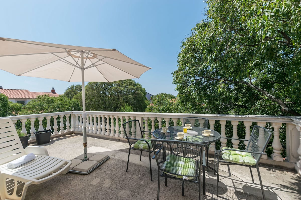 A balcony with a table and chairs, a large umbrella, and potted plants.