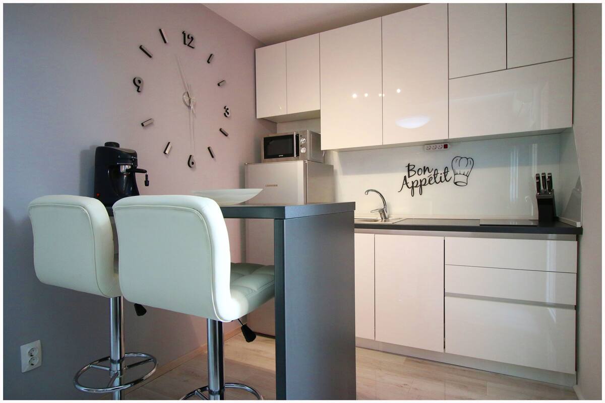 Una cocina moderna con armarios blancos, un microondas, una cafetera y un reloj en la pared.