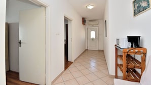 A hallway with a tiled floor, a wooden bench, a microwave, and a coffee maker on a table.