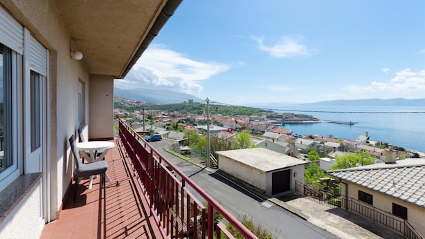 A balcony with a view of a coastal town, a clear sky, and a calm sea.