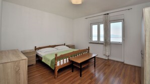 A bedroom with a wooden bed, a wooden bench, a nightstand, a dresser, and a window with curtains.