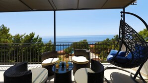 A balcony with wicker furniture, a hanging chair, and a view of the sea. - Apartments Redstone Luxury Apartments (Sveta Nedjelja)