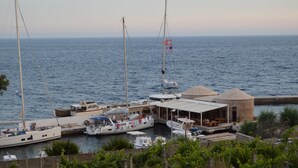 A marina with several boats docked, a small building with a thatched roof, and a view of the sea. - Apartments Redstone Luxury Apartments (Sveta Nedjelja)