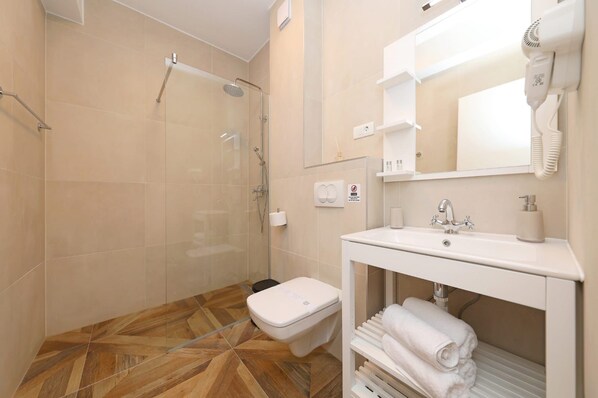 Un baño moderno con cabina de ducha de vidrio, un lavamanos blanco con espejo arriba y piso de madera.