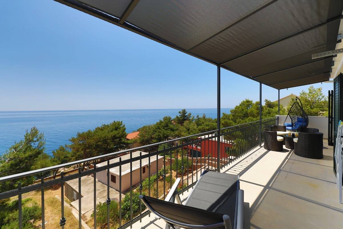 A balcony with a view of the sea, outdoor furniture, and a hanging chair.