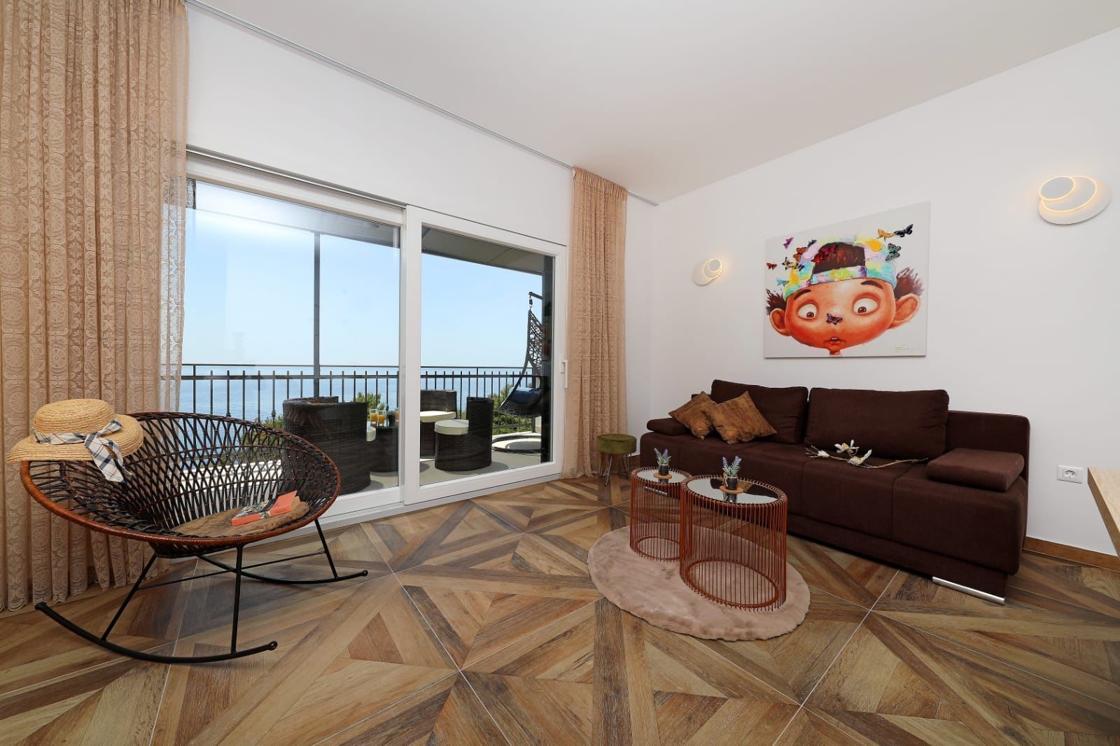 A living room with a sofa, a chair, a table, and a large window with a view of the sea.