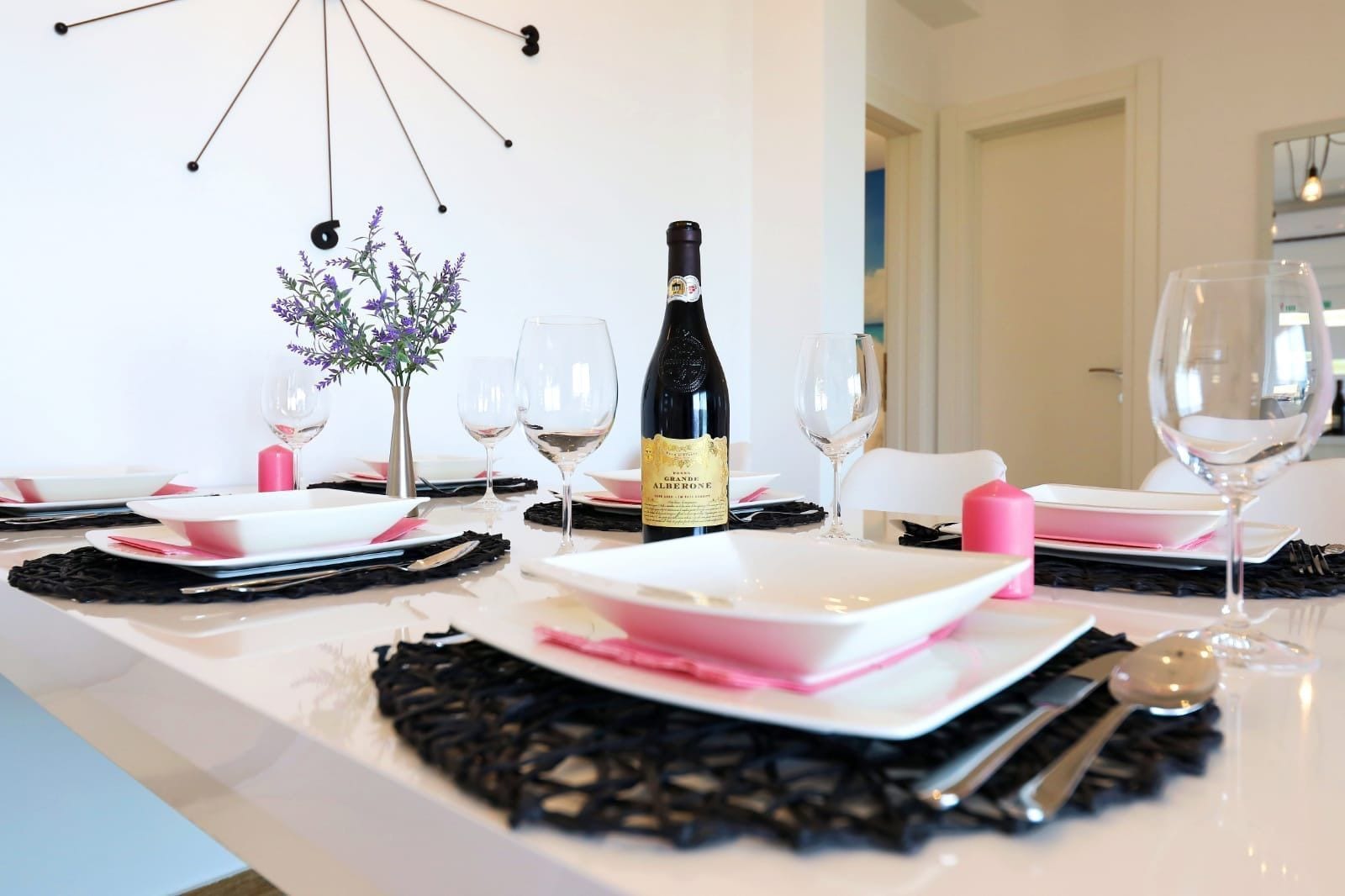 A dining table set with pink and white plates, a bottle of wine, and a vase with purple flowers.
