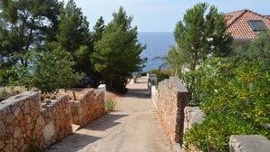 A stone pathway leading to a house with a tiled roof, surrounded by trees and a view of the sea. - Apartments Redstone Luxury Apartments (Sveta Nedjelja)