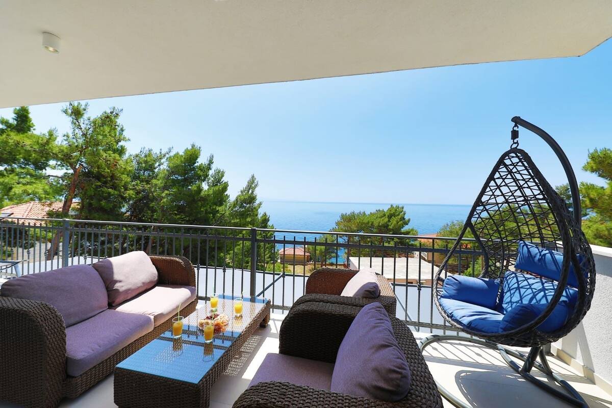 A balcony with wicker furniture, a hanging chair, and a table with breakfast items.