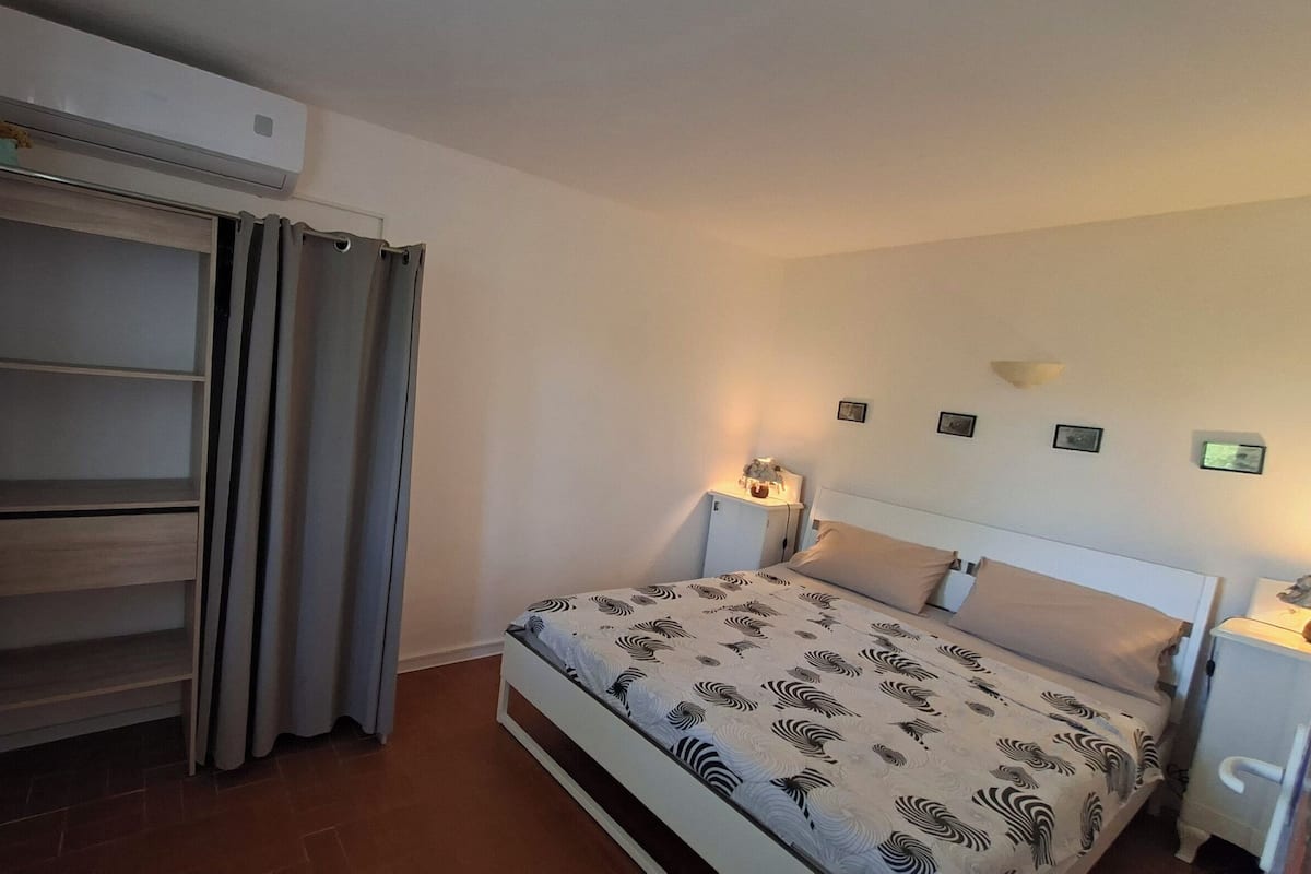 Ein Schlafzimmer mit einem Bett, einem Nachttisch mit Lampe, einem Kleiderschrank und einer Wand-Klimaanlage.