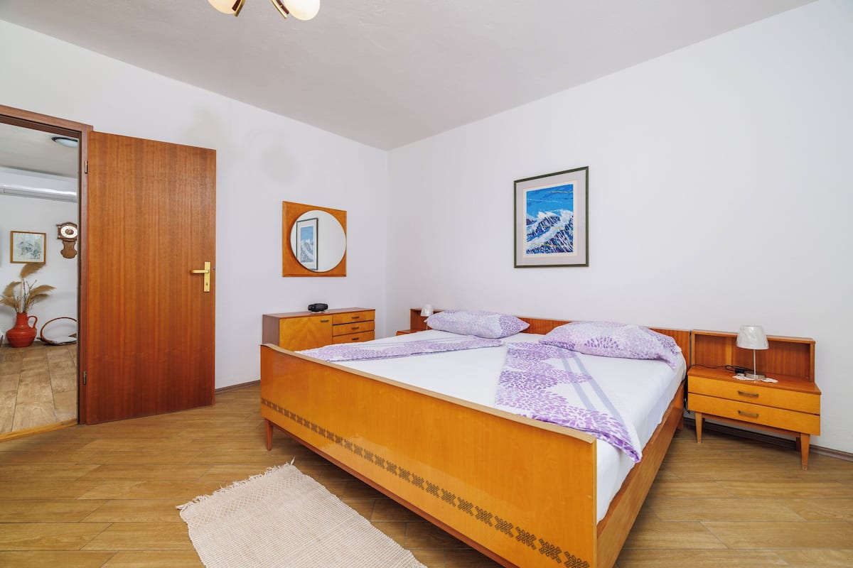Un dormitorio con una cama de madera, una mesita de noche, un tocador, un espejo y un cuadro en la pared.