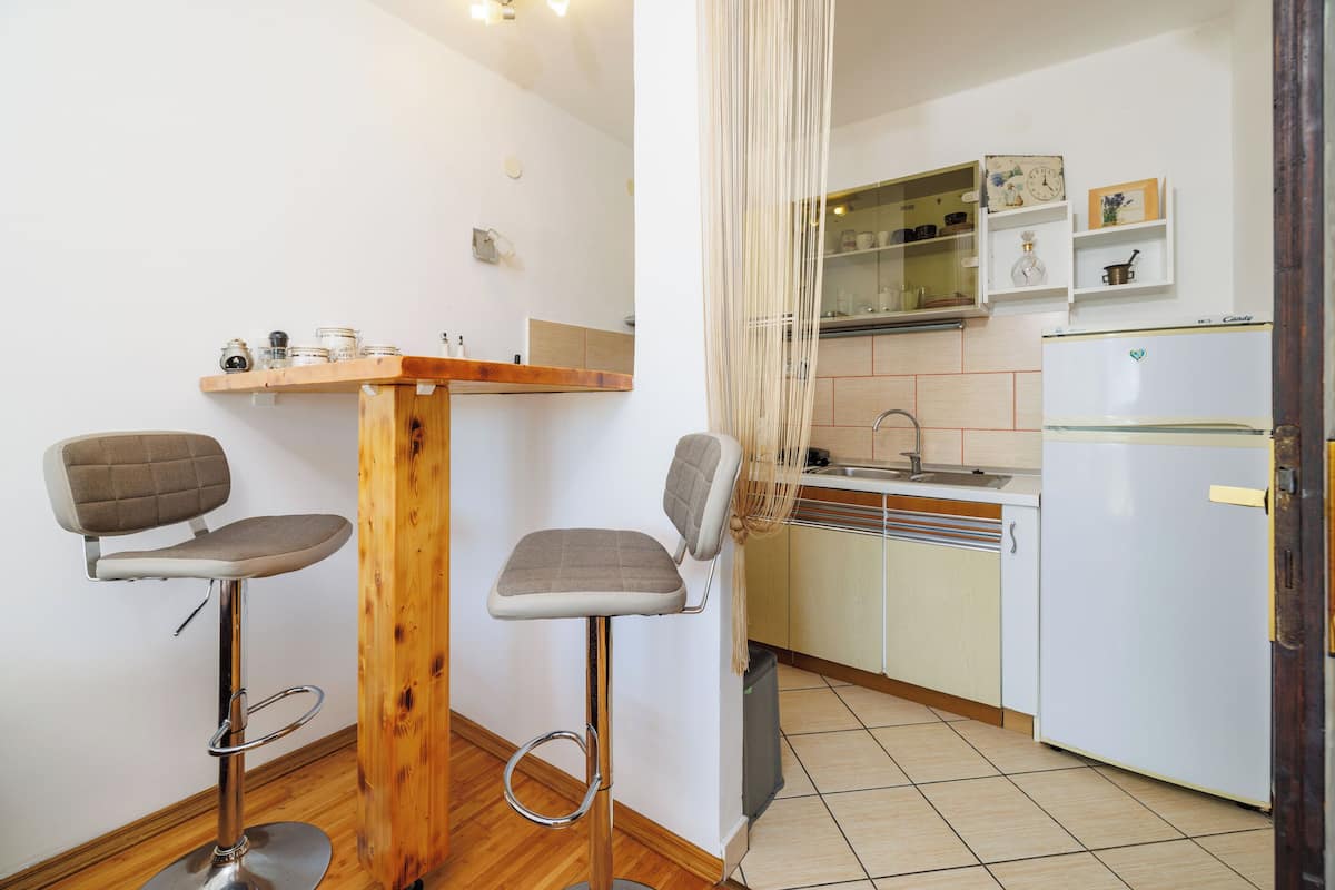 Una pequeña cocina con un taburete de madera y dos taburetes más, un refrigerador y un lavamanos.