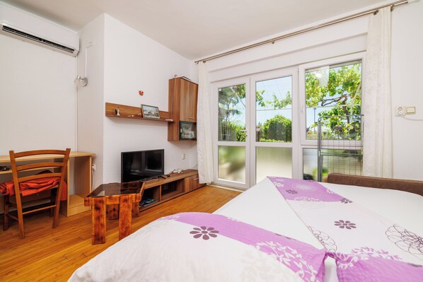 A bedroom with a bed, a desk, a television, and a window with a view of greenery. - Apartments Jadrana (Novi Vinodolski)