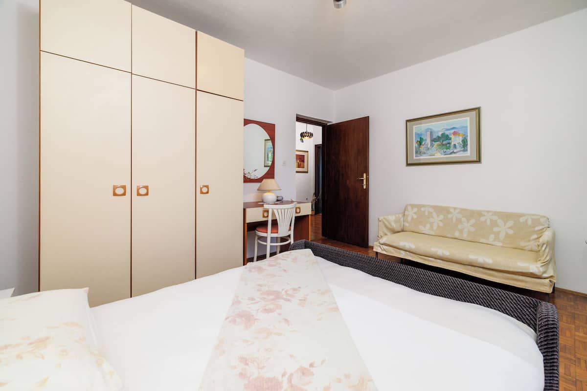 Un dormitorio con cama, armario, escritorio con silla, sofá, espejo y un cuadro en la pared.