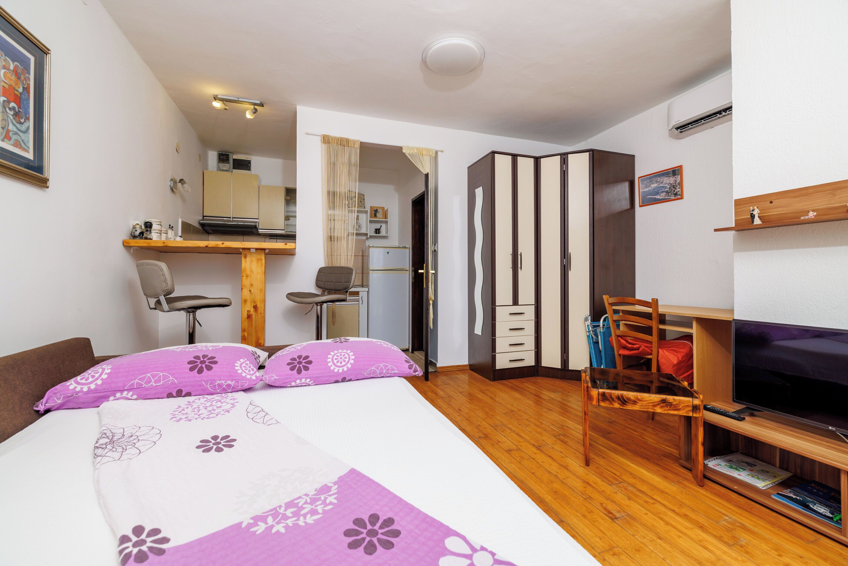 Un dormitorio con cama, televisor, una silla de madera, escritorio y armario.