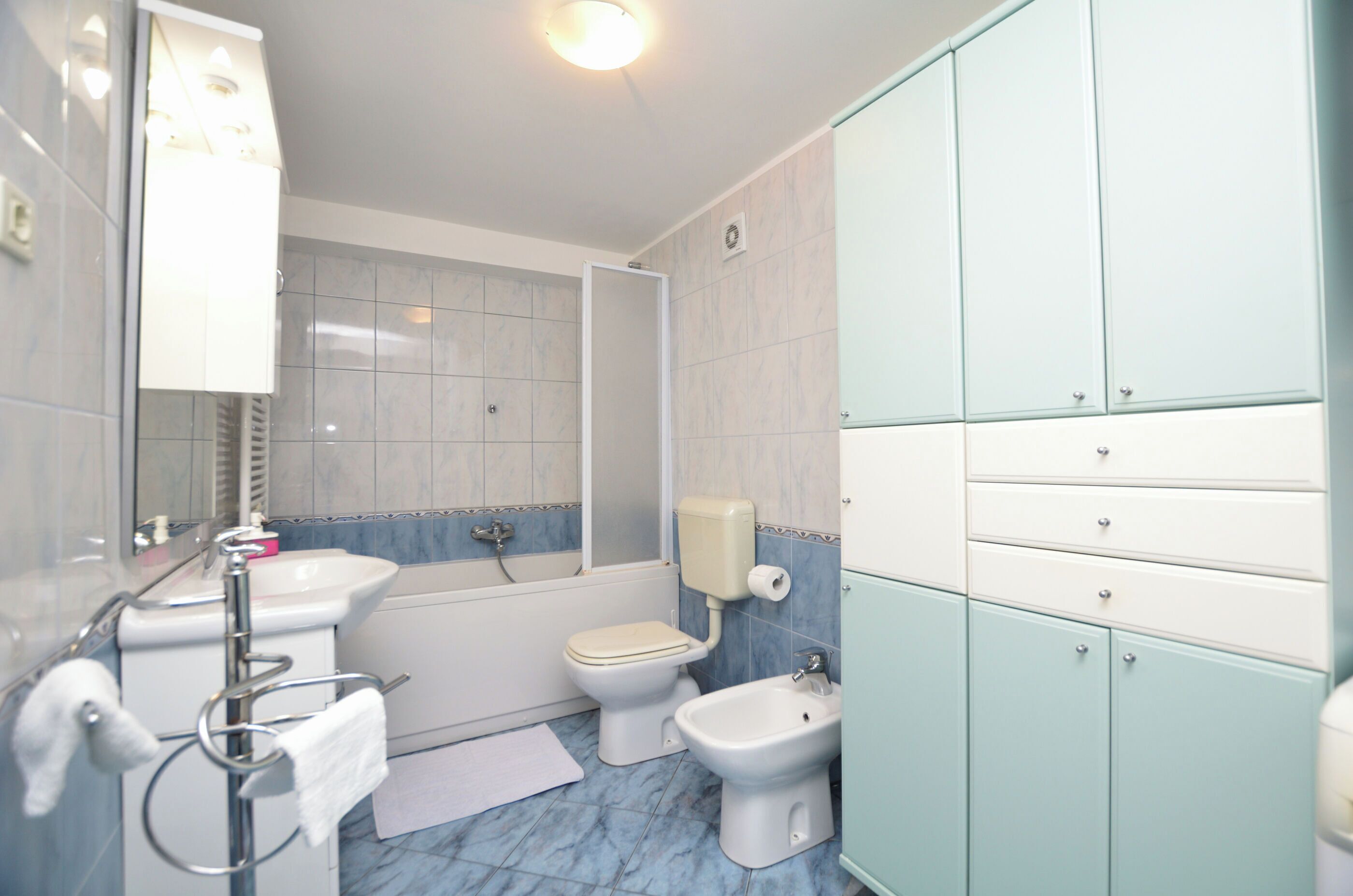 A bathroom with a toilet, bidet, sink, and cabinet.