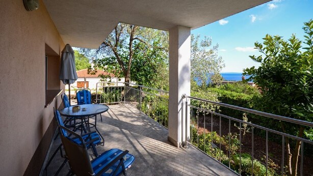 A balcony with a table and chairs, a view of the sea, and a garden area. - Apartment Visnja (Rijeka)