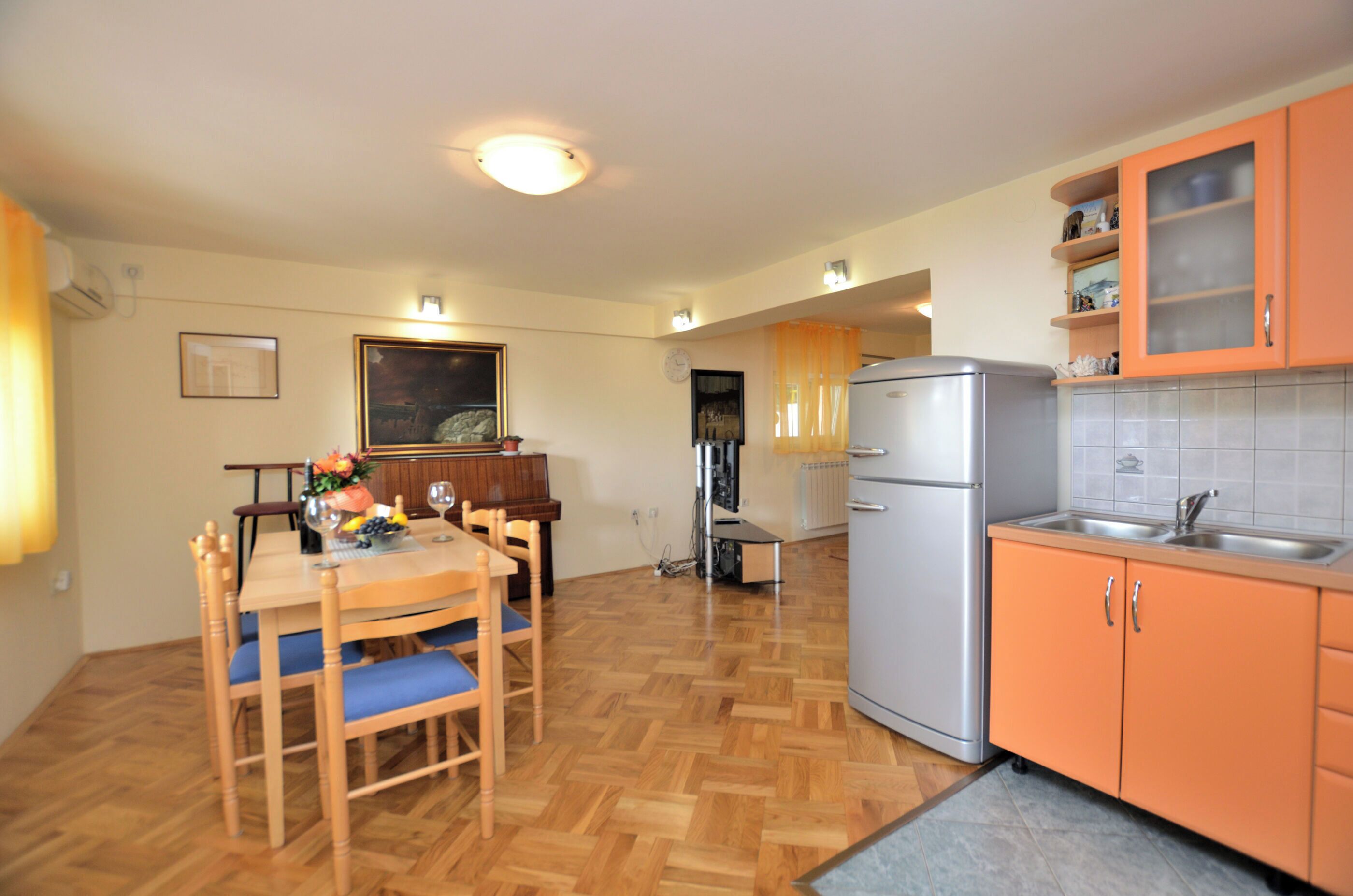 A compact kitchen with a refrigerator, orange cabinets, and a dining area with wooden chairs and a table.