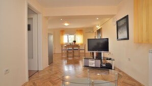 A spacious living room with a wooden floor, a glass coffee table, a flat-screen TV, and a dining area with a table and chairs. - Apartment Visnja (Rijeka)